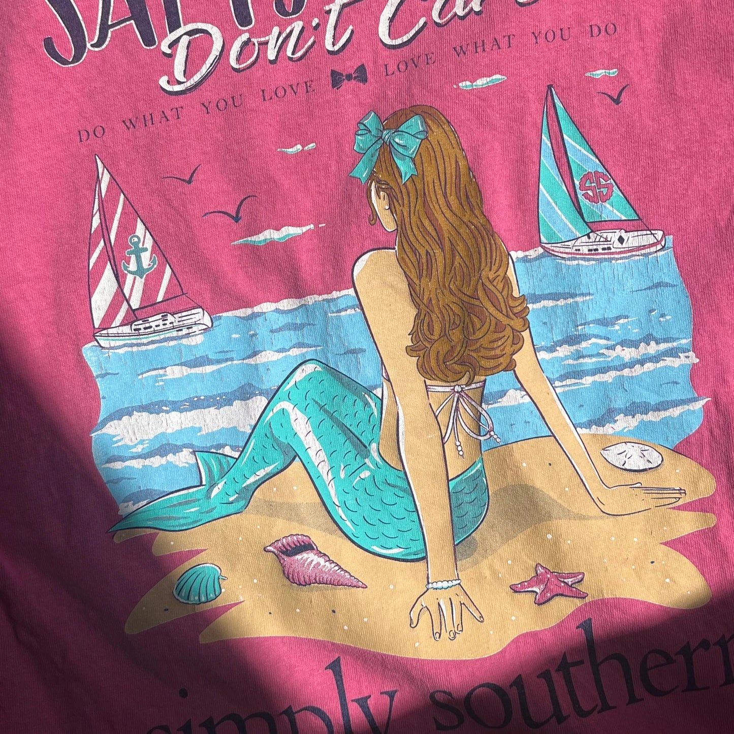 A mermaid graphicsand beach scene on a light pink t-shirt