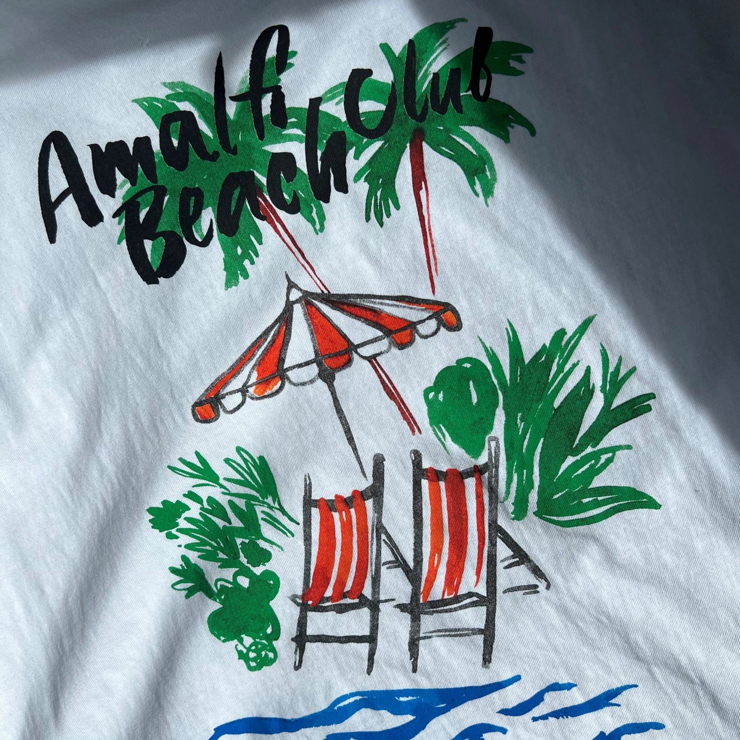 100% cotton White T-shirt with Amalfi Beach Club text, beach chairs, and palm trees