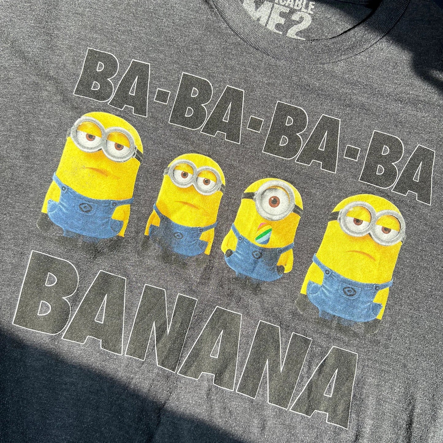 Four yellow minions and text 'BA-BA-BA-BA BANANA' on a dark grey t-shirt