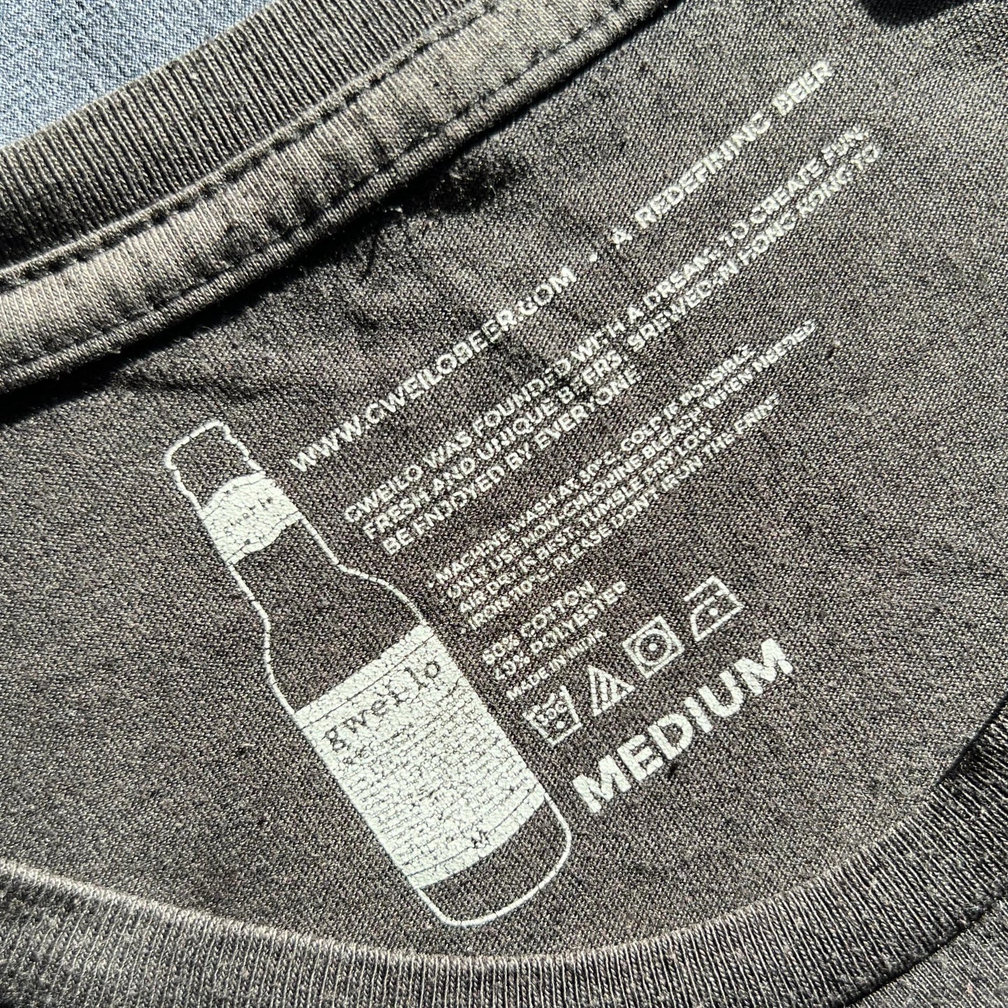 Black t-shirt with printed beer bottle design and text on a carelabel surface