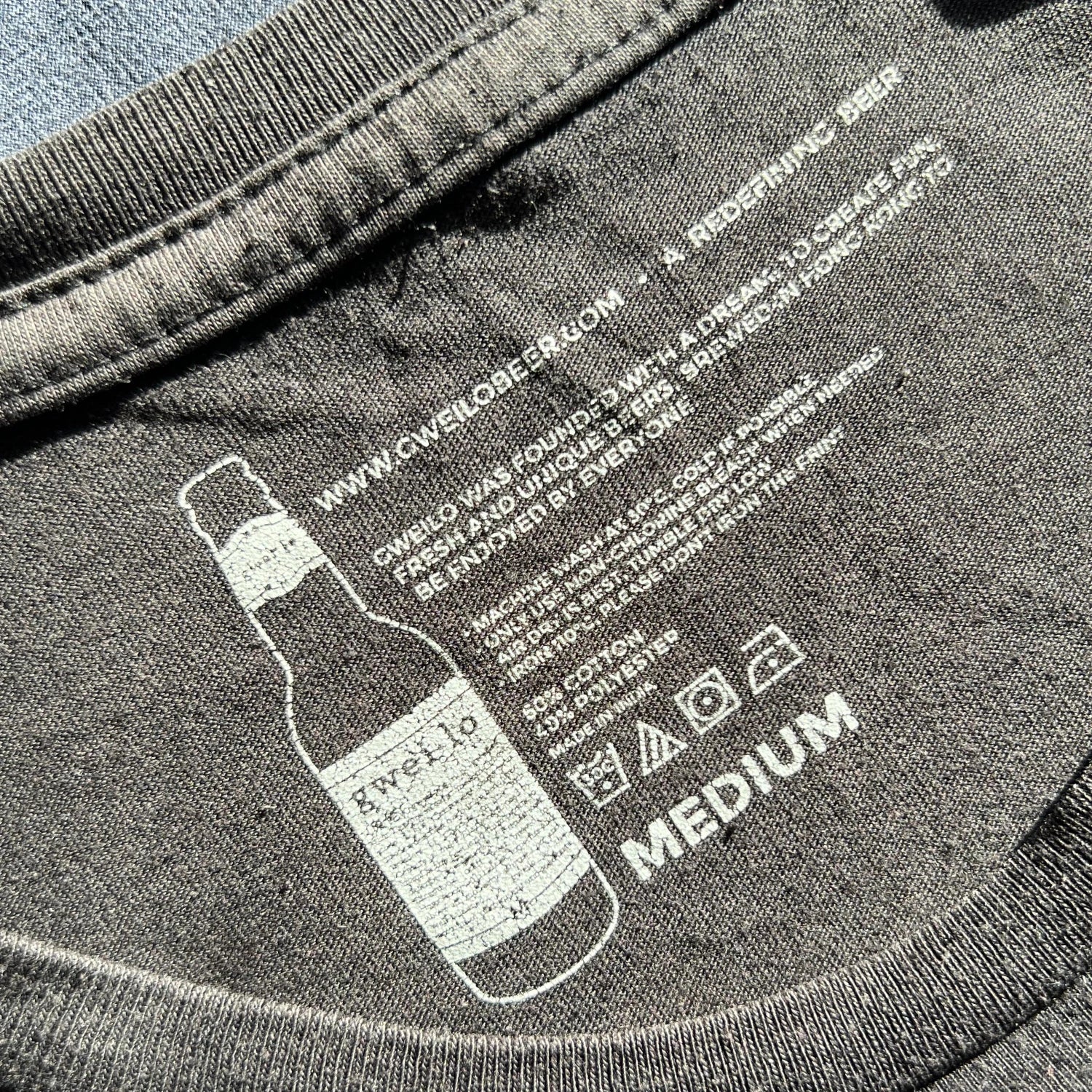 Black t-shirt with printed beer bottle design and text on a carelabel surface