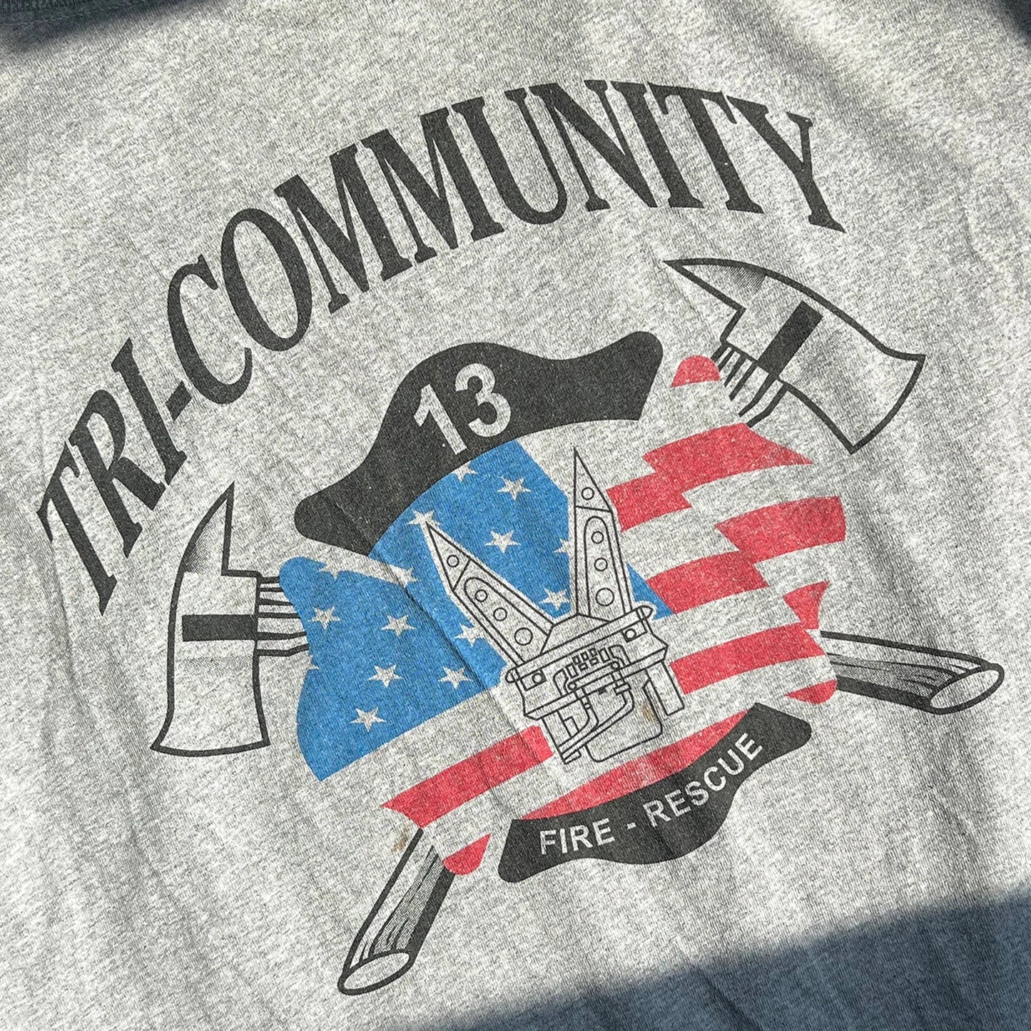 Light_Heather_Grey_t-shirt with 'Tri-Community Fire Rescue' graphic design featuring axes, an American flag, and a building.