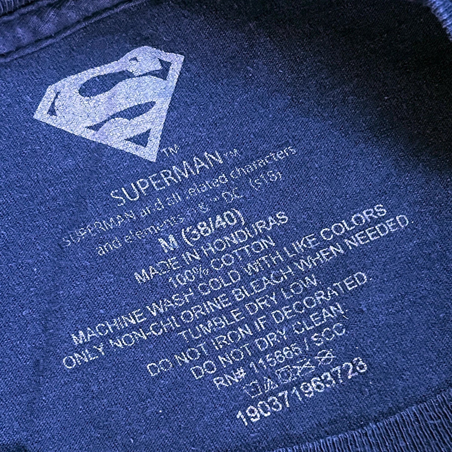 Superman logo on a dark blue t-shirt with text about garment care and origin